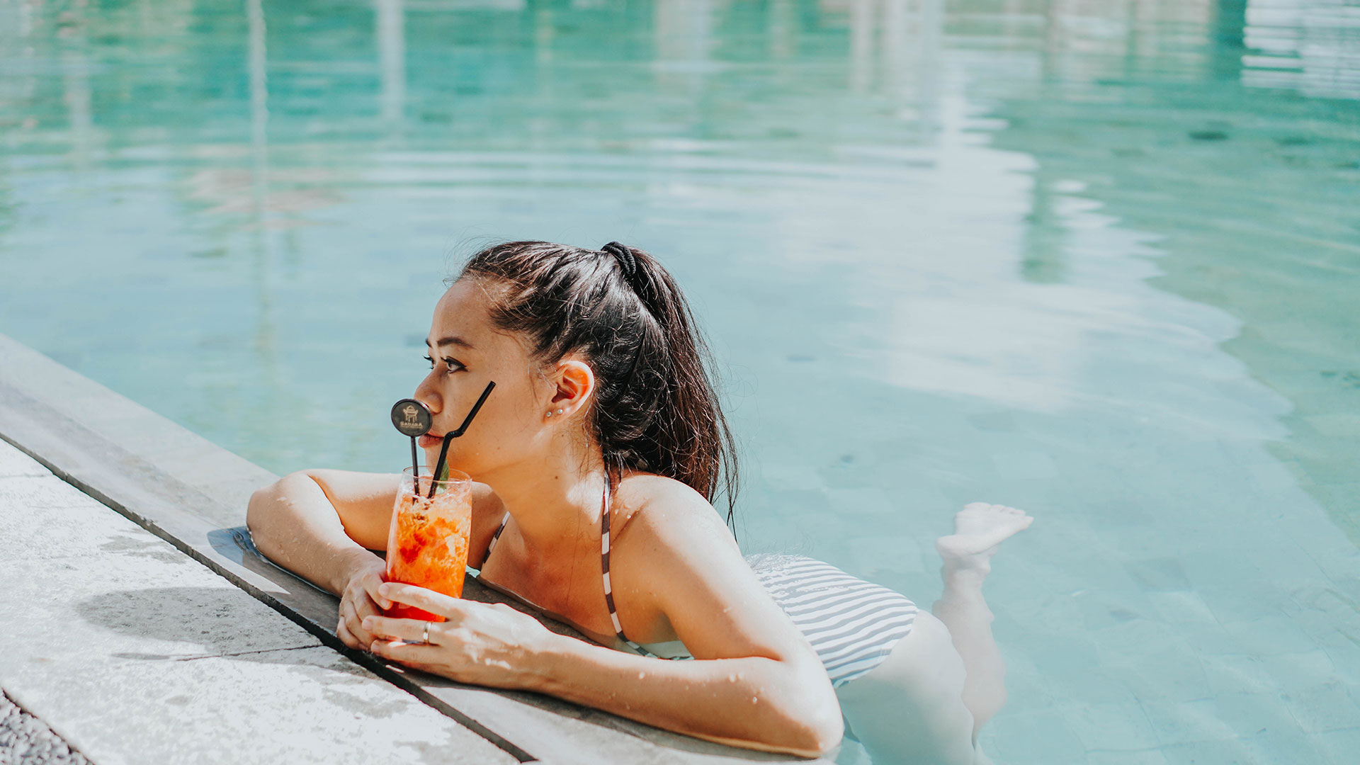 a woman in a bikini drinking from a straw in a pool at The  Mark at 2600